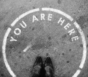 Standortbestimmung. 2 Füße stehen auf Asphalt in einem Kreis mit der aufgesprühten Schrift: "You are here"